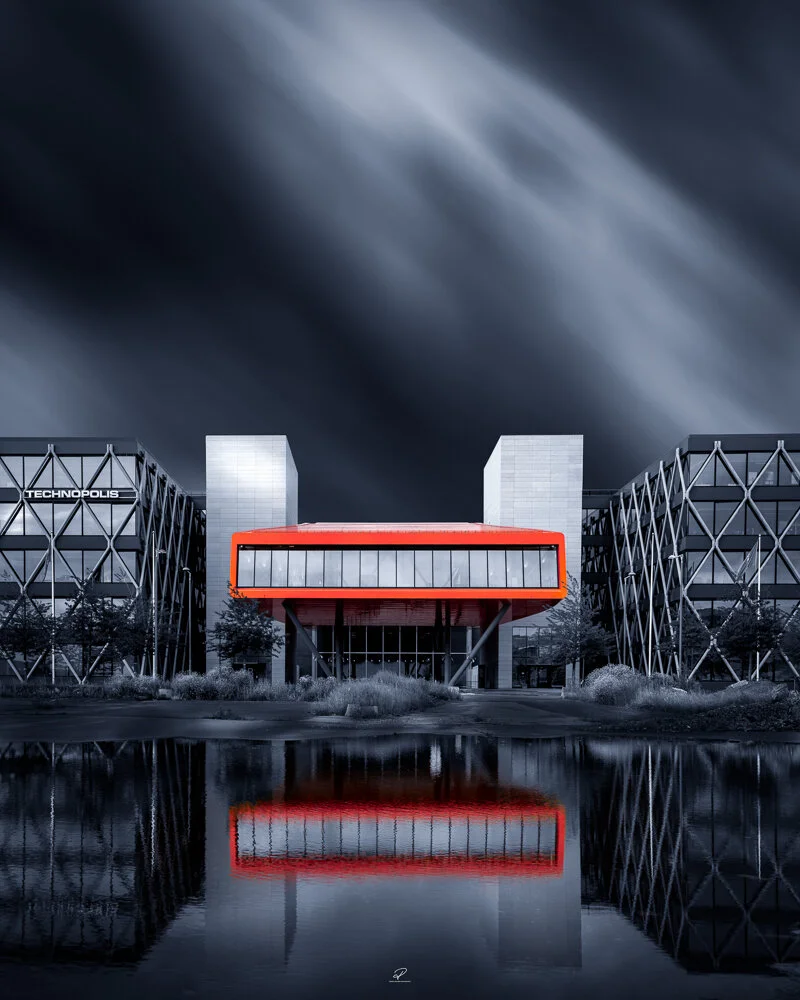 Modern building with geometric design, glass facade, and a red overhang, reflected in a body of water, with dark stormy sky in background. Technopolis, Fornebu. Arkitektur foto Oslo.