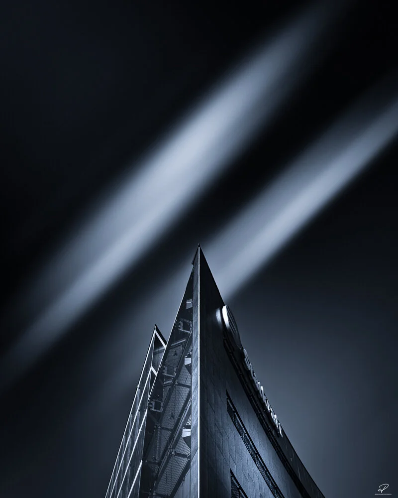 Nighttime photo of a modern high-rise building with illuminated beams of light projected into the sky. Arkitektur foto Oslo.