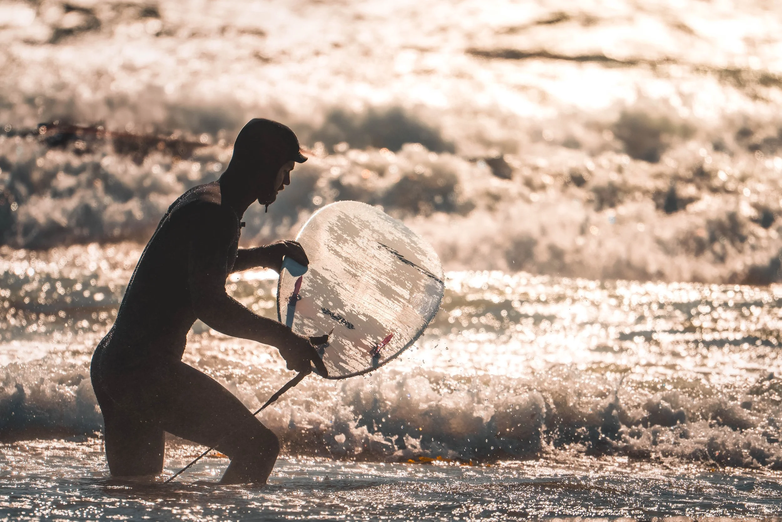 A surfer preparing to enter the ocean during golden hour at Saltstein. Warm light, textures, and motion create a cinematic coastal photography scene.
