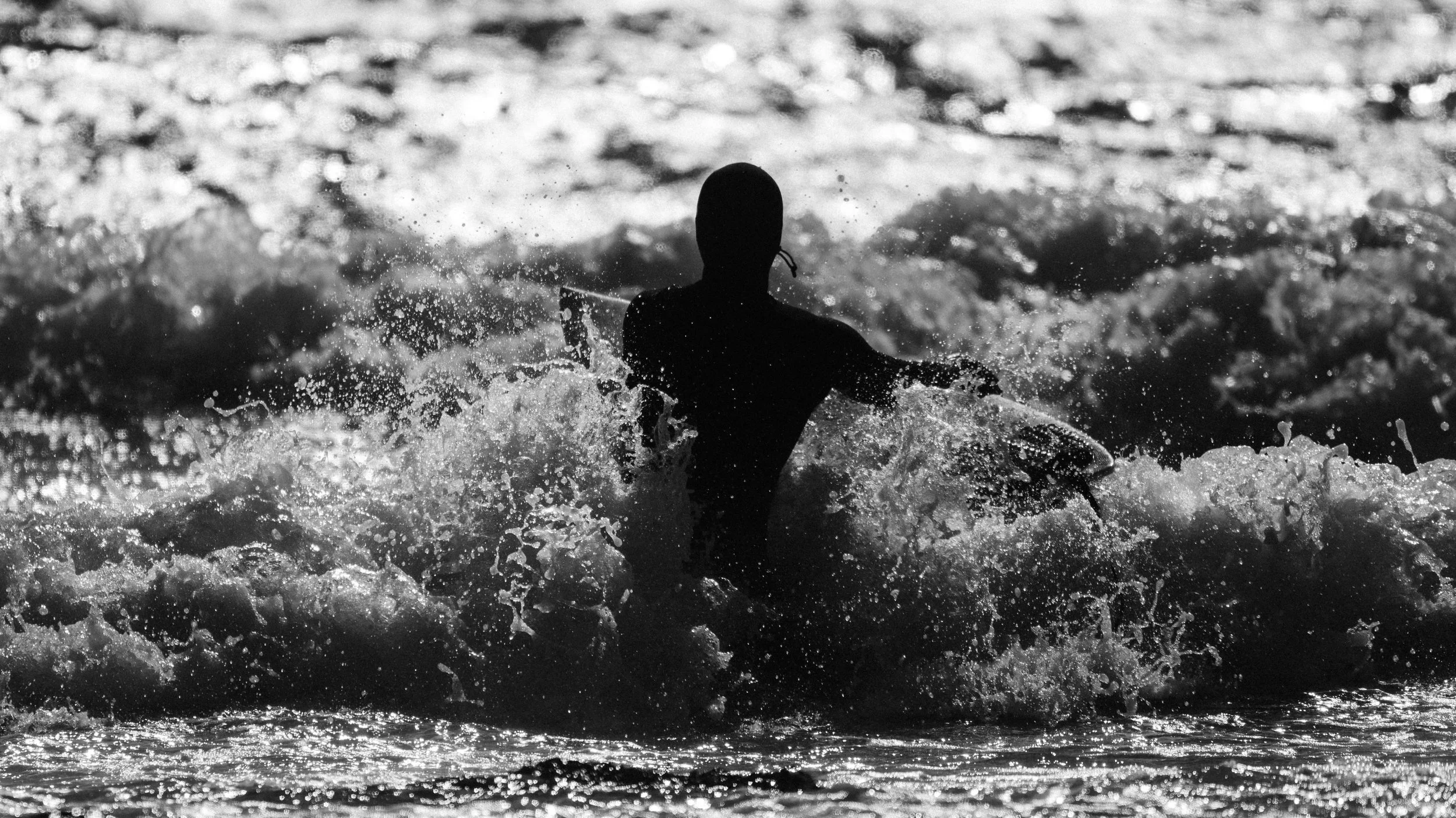 Minimalist black and white photograph of a surfer watching waves at Saltstein beach in Norway. Capturing atmosphere, movement, and solitude in coastal landscape photography.