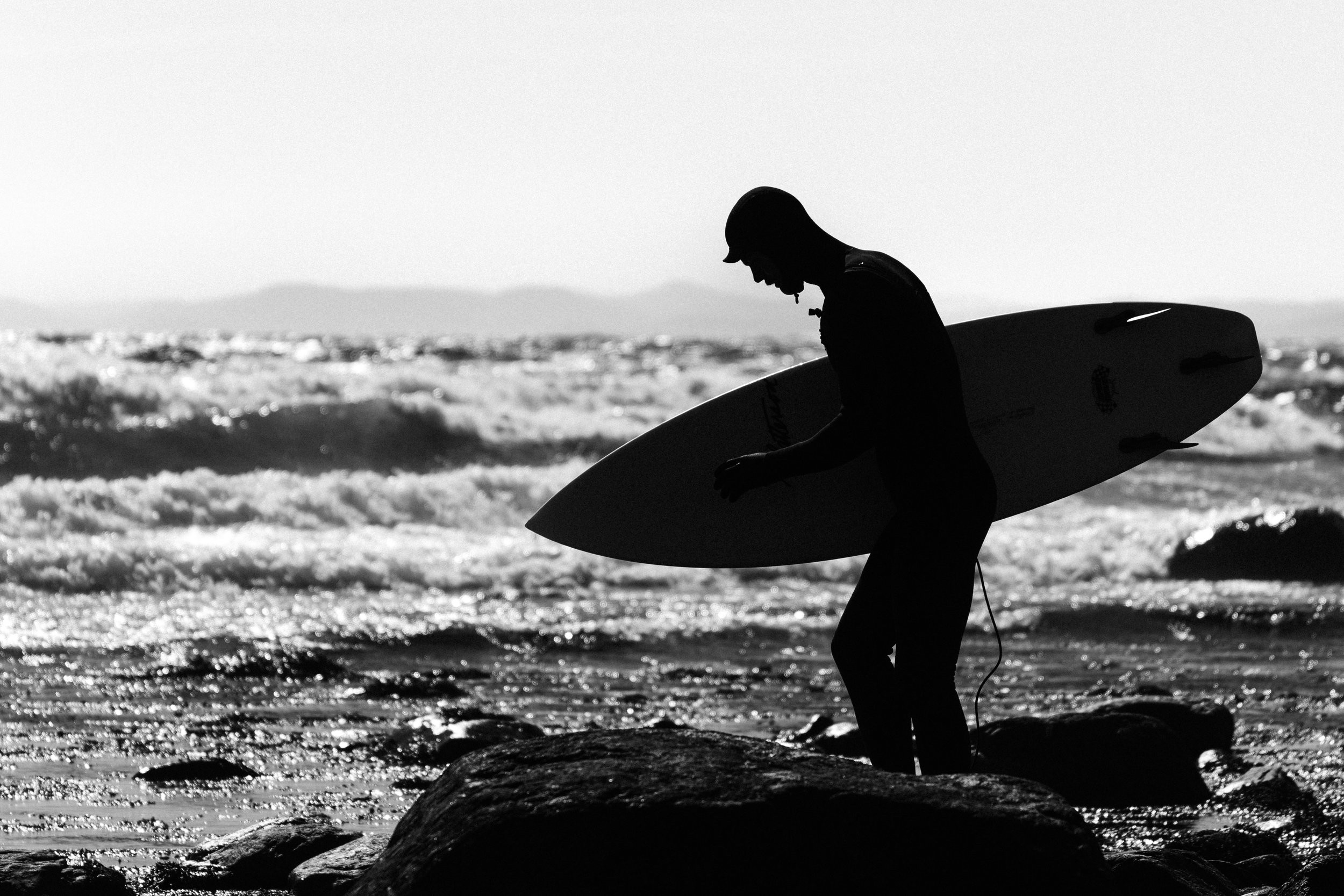 Minimalist black and white photograph of a surfer about to enter the water at Saltstein beach in Norway. Capturing atmosphere, movement, and solitude in coastal landscape photography.