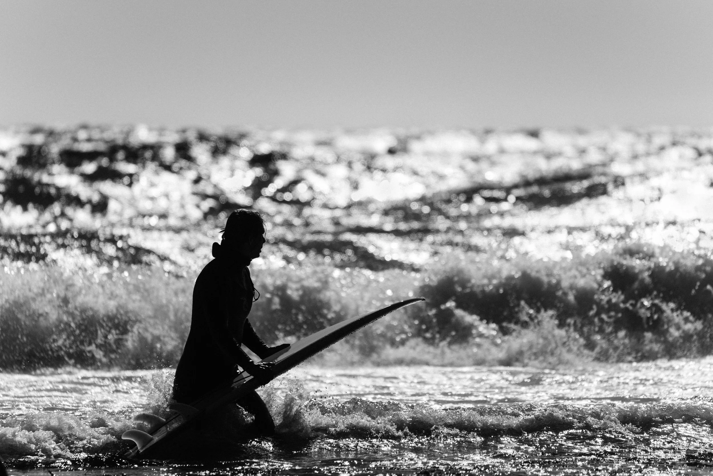 Minimalist black and white photograph of a surfer watching waves at Saltstein beach in Norway. Capturing atmosphere, movement, and solitude in coastal landscape photography.