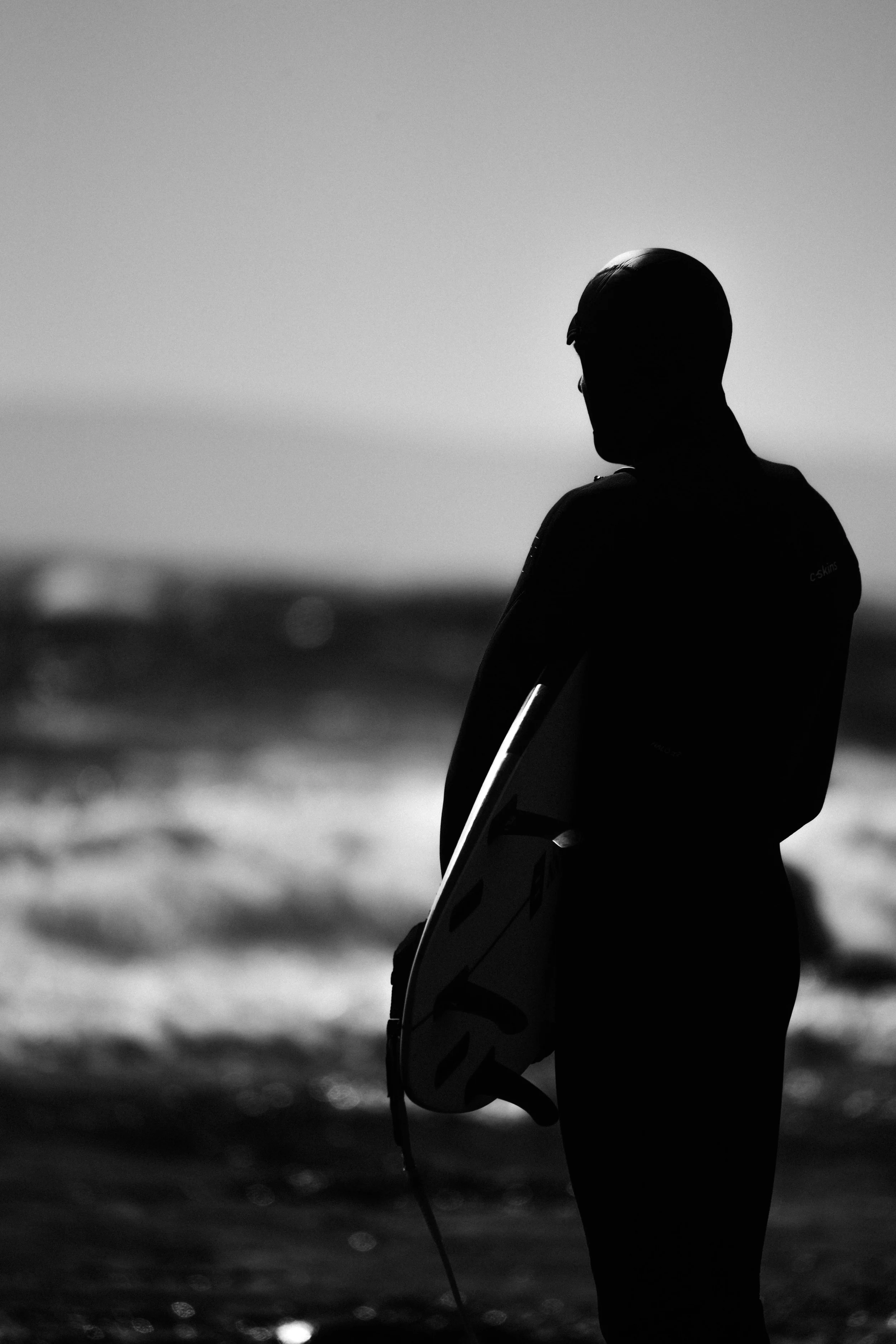 Minimalist black and white photograph of a surfer watching waves at Saltstein beach in Norway. Capturing atmosphere, movement, and solitude in coastal landscape photography.