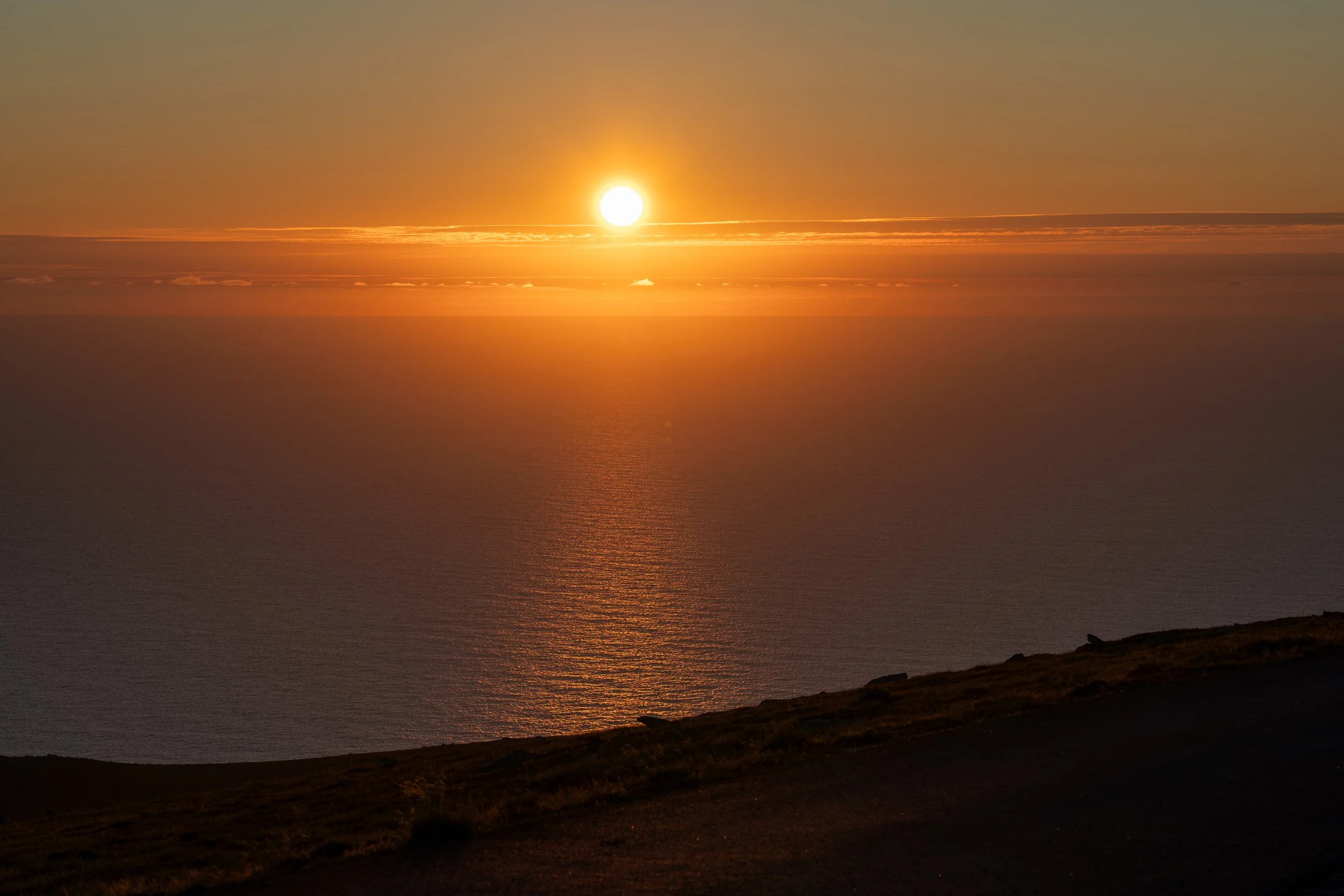 Sunset over the ocean with reflections on the water, viewed from a hillside.