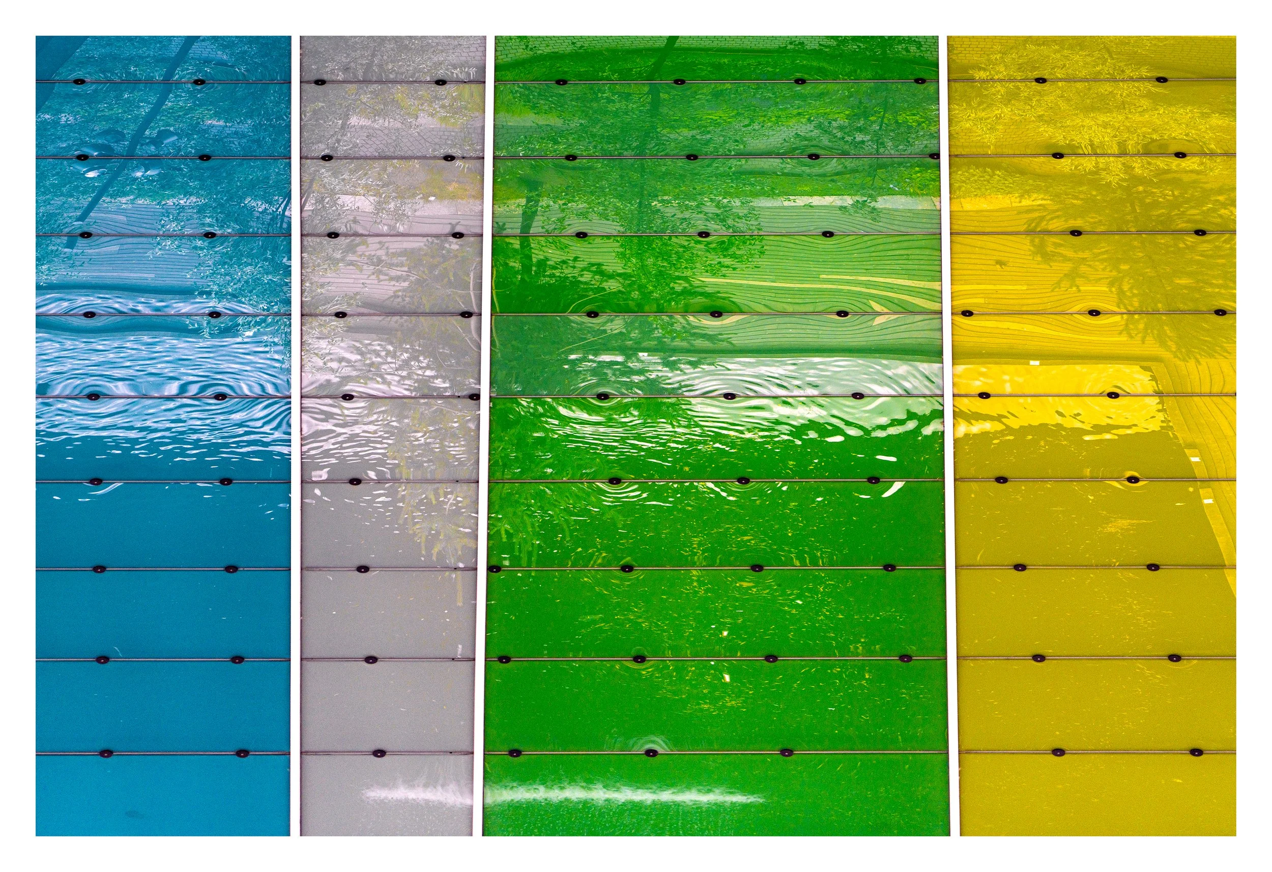 Close-up of a multi-colored, segmented glass or plastic surface, with reflected trees and sky visible through each segment in blue, gray, green, and yellow sections. Barcode Oslo. Arkitektur foto.