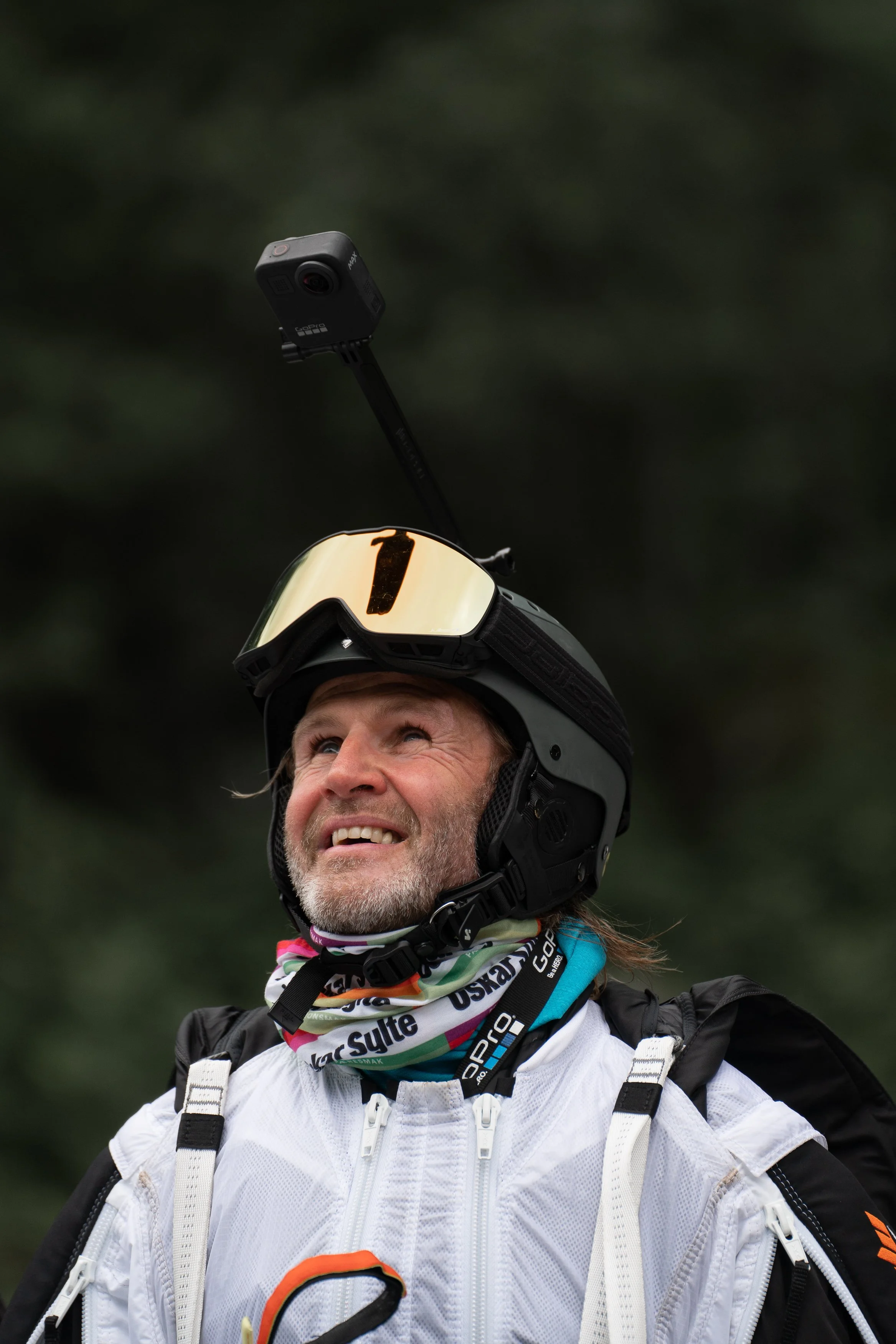 Man in off-road gear and helmet with a GoPro camera mounted on a stick, smiling and looking up. Forest background. Wingsuit.