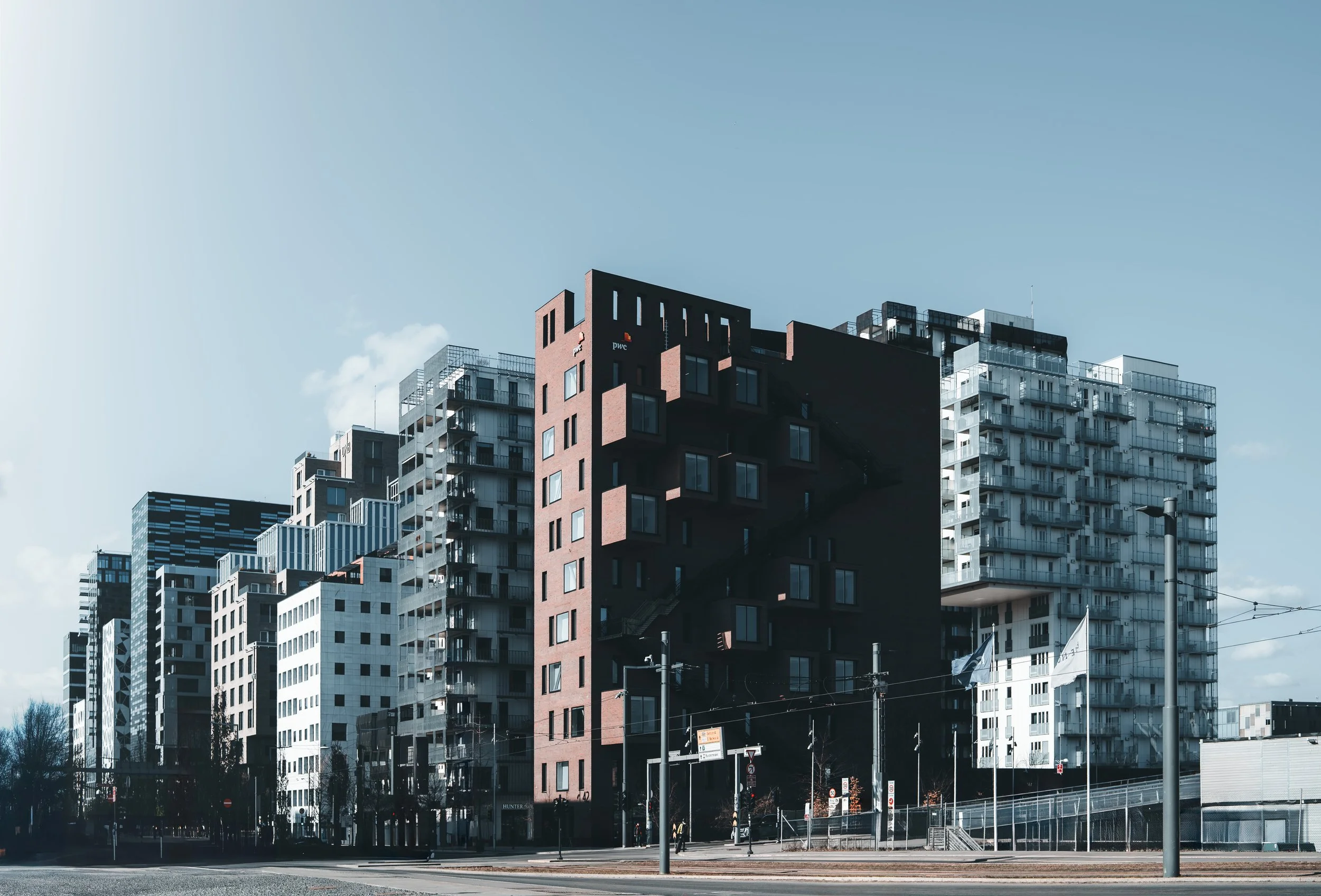 Modern high-rise buildings with glass balconies and dark exteriors in an urban cityscape under a clear blue sky. Arkitektur foto oslo. Barcode.
