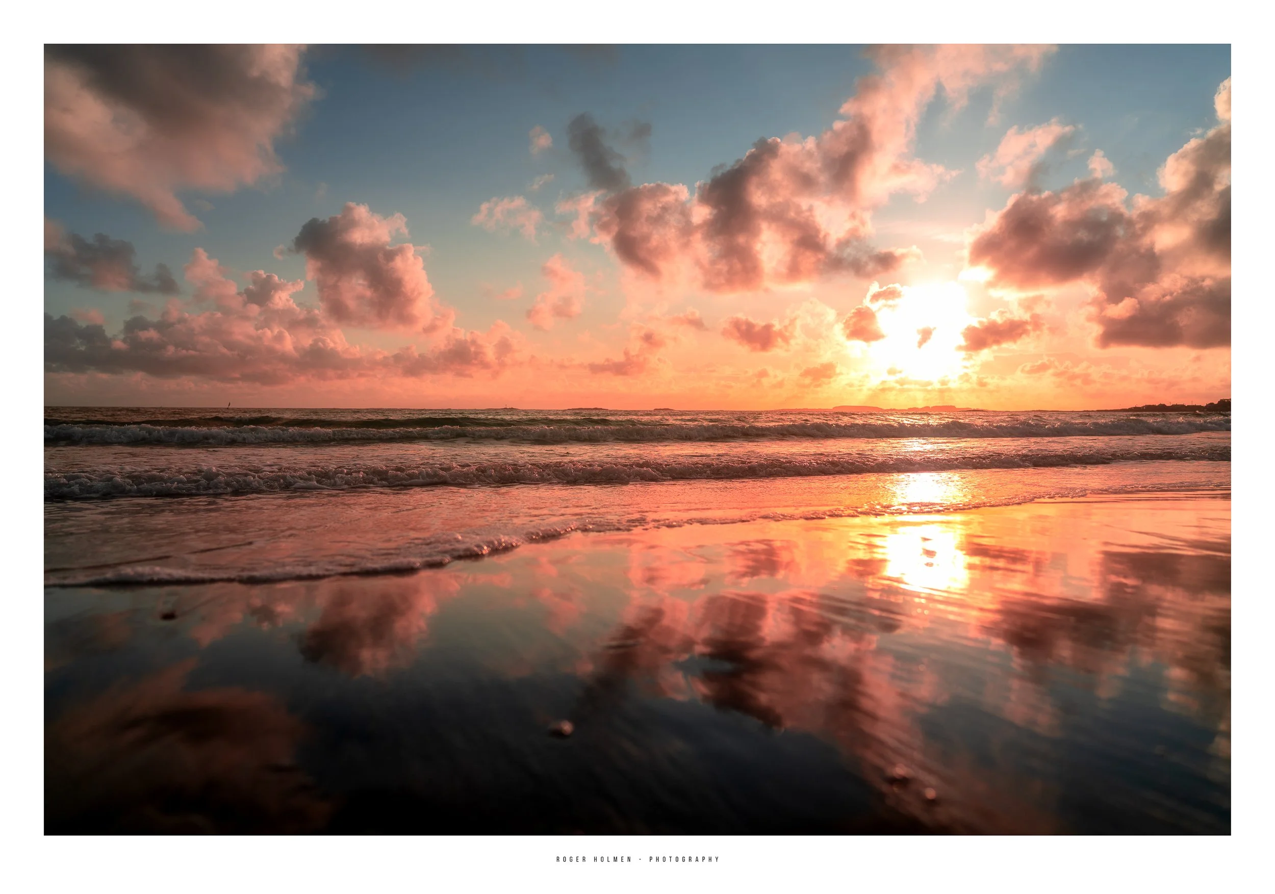 Sunset over the ocean with pink and orange clouds and waves hitting the shore, reflecting the colorful sky on wet sand.