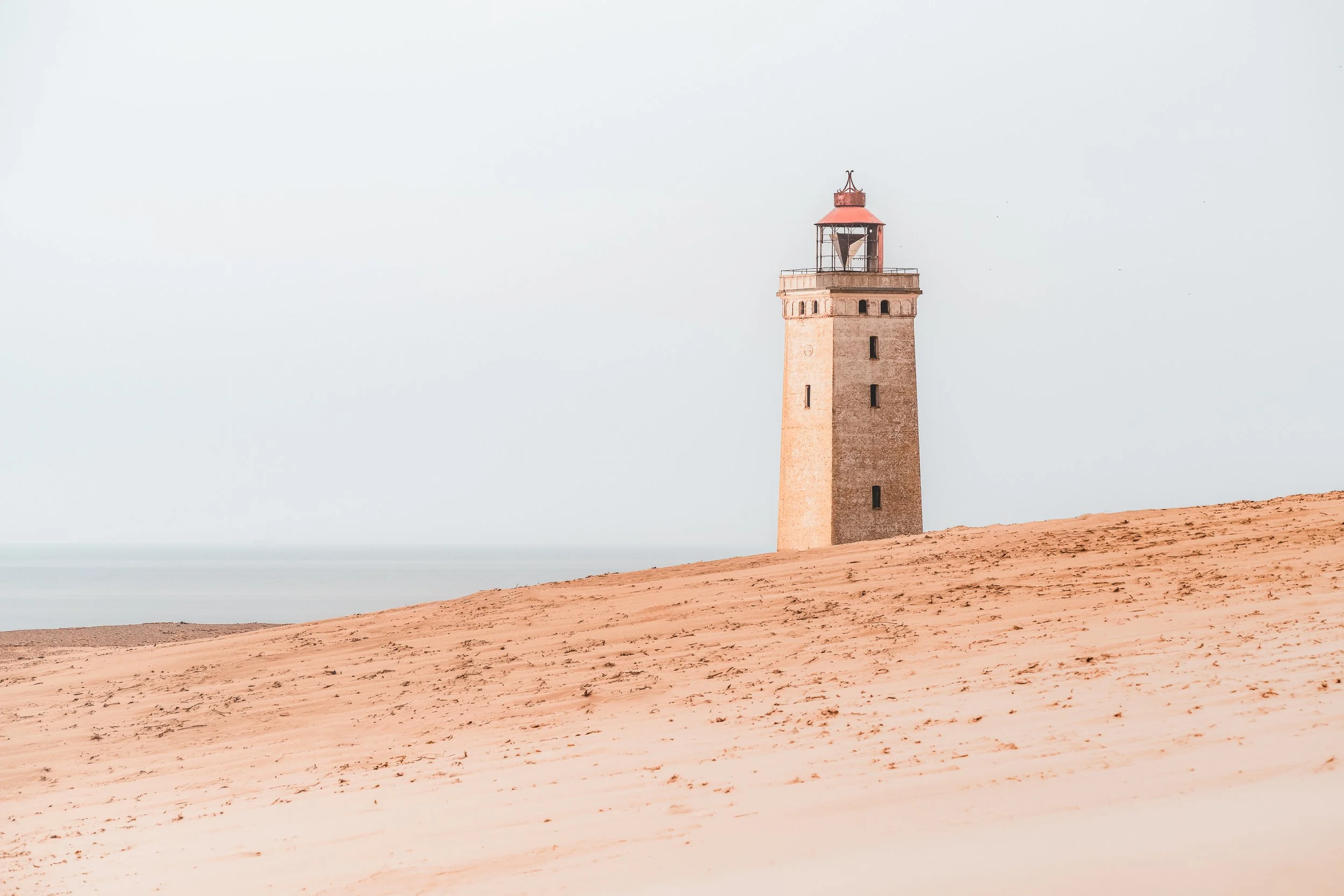 A lighthouse on a sandy beach with a hazy sky in the background.
