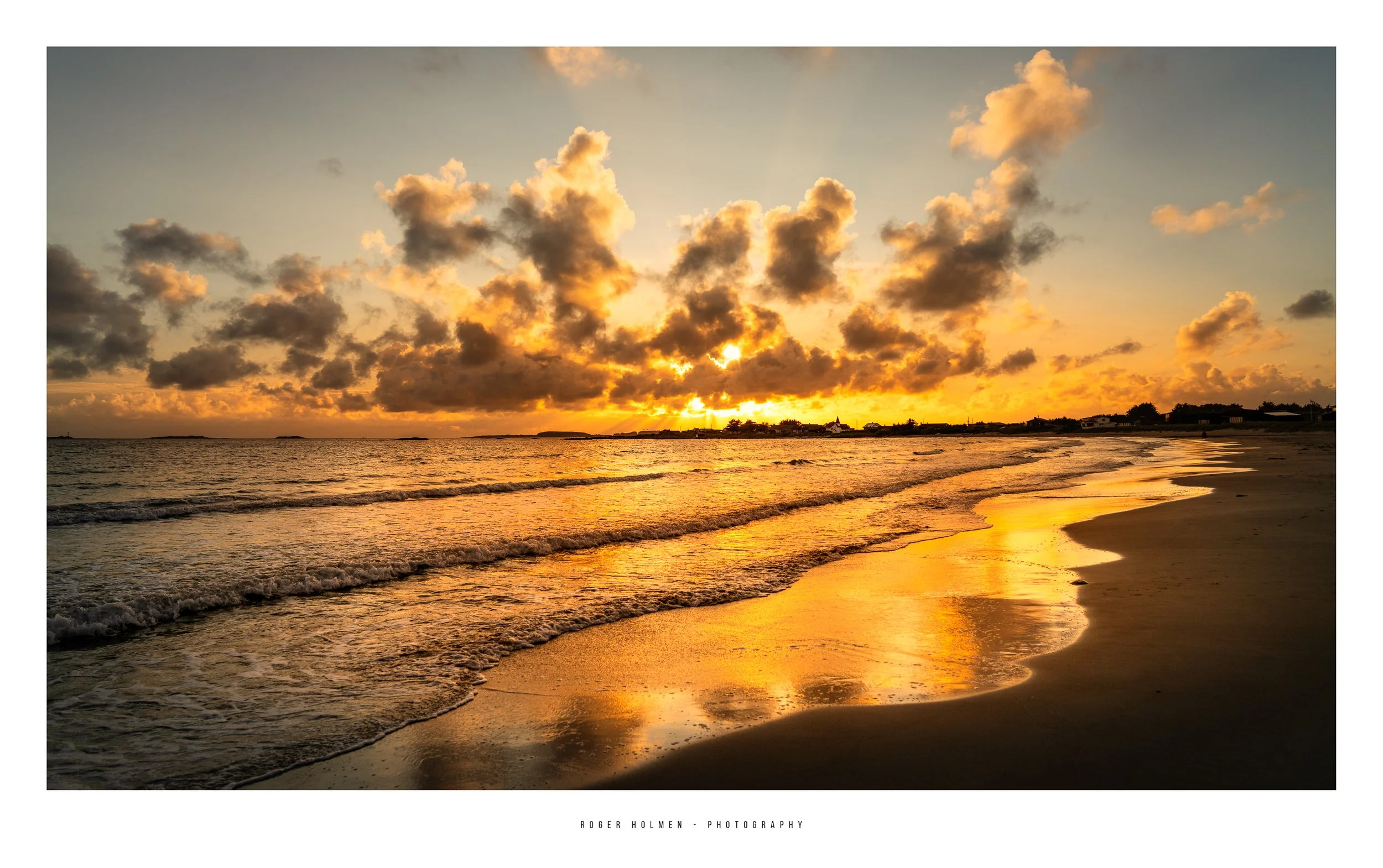 Sunset over a beach with clouds, reflecting orange and yellow hues on the wet sand and ocean waves.
