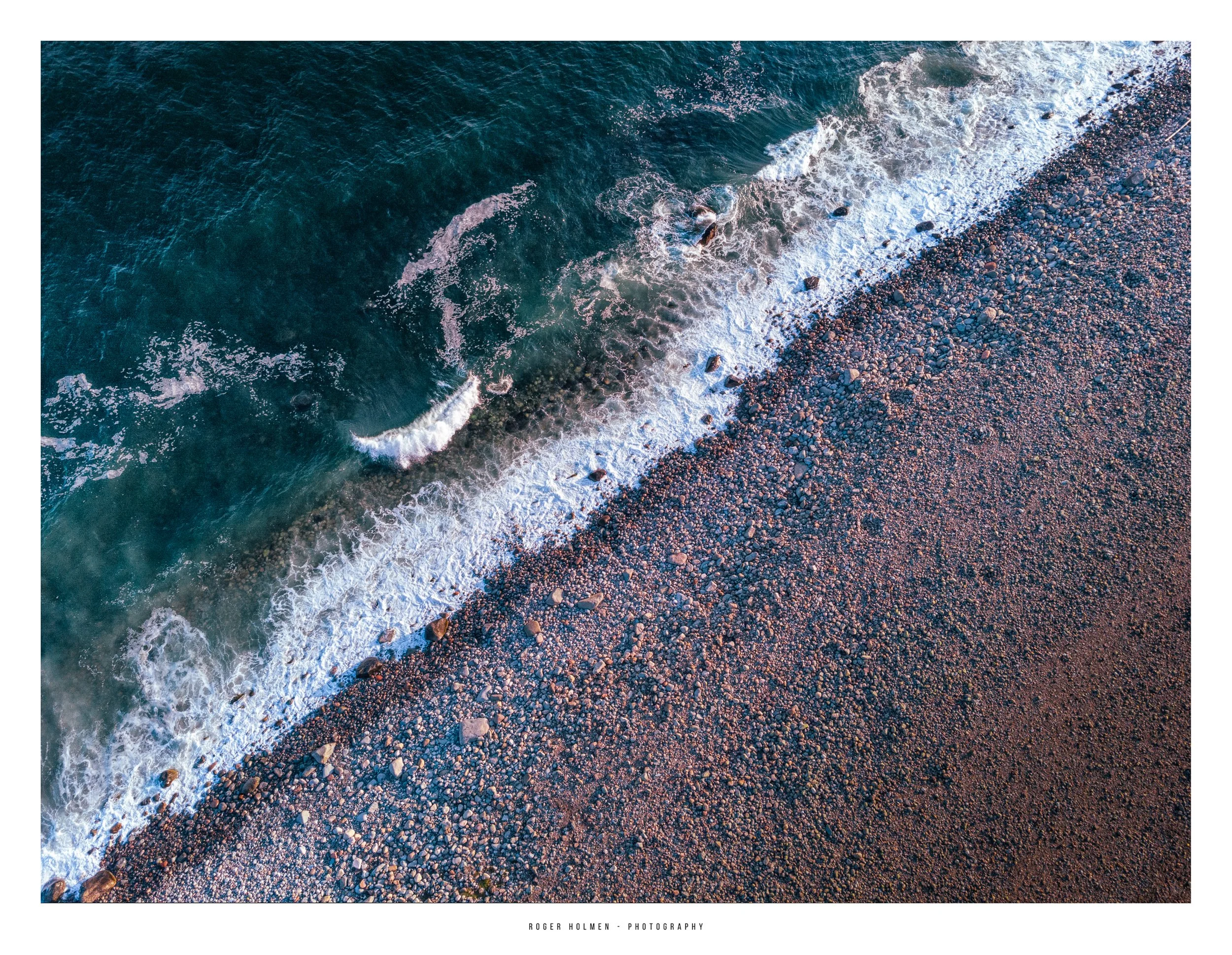 Aerial view of a pebble beach with waves washing onto the shore.