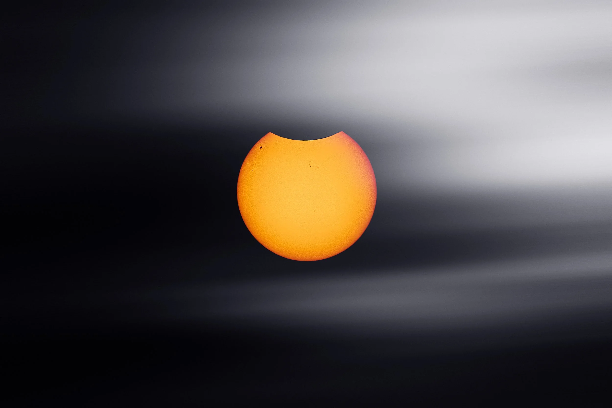 A close-up of an orange, spherical object with a bite taken out of its top, set against a blurred black and gray background.
