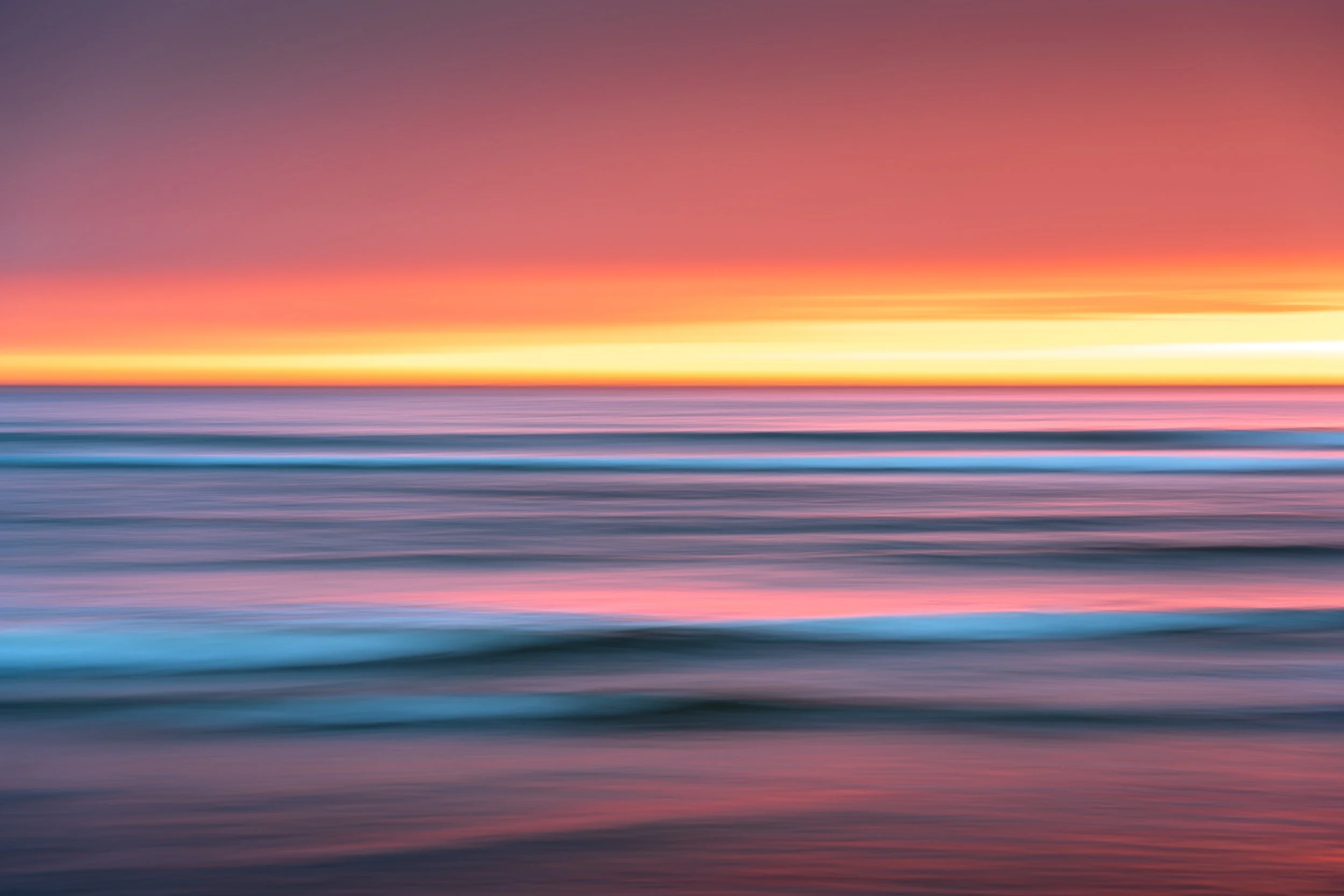 Blurred image of ocean waves during a colorful sunset or sunrise with shades of pink, orange, purple, and blue.