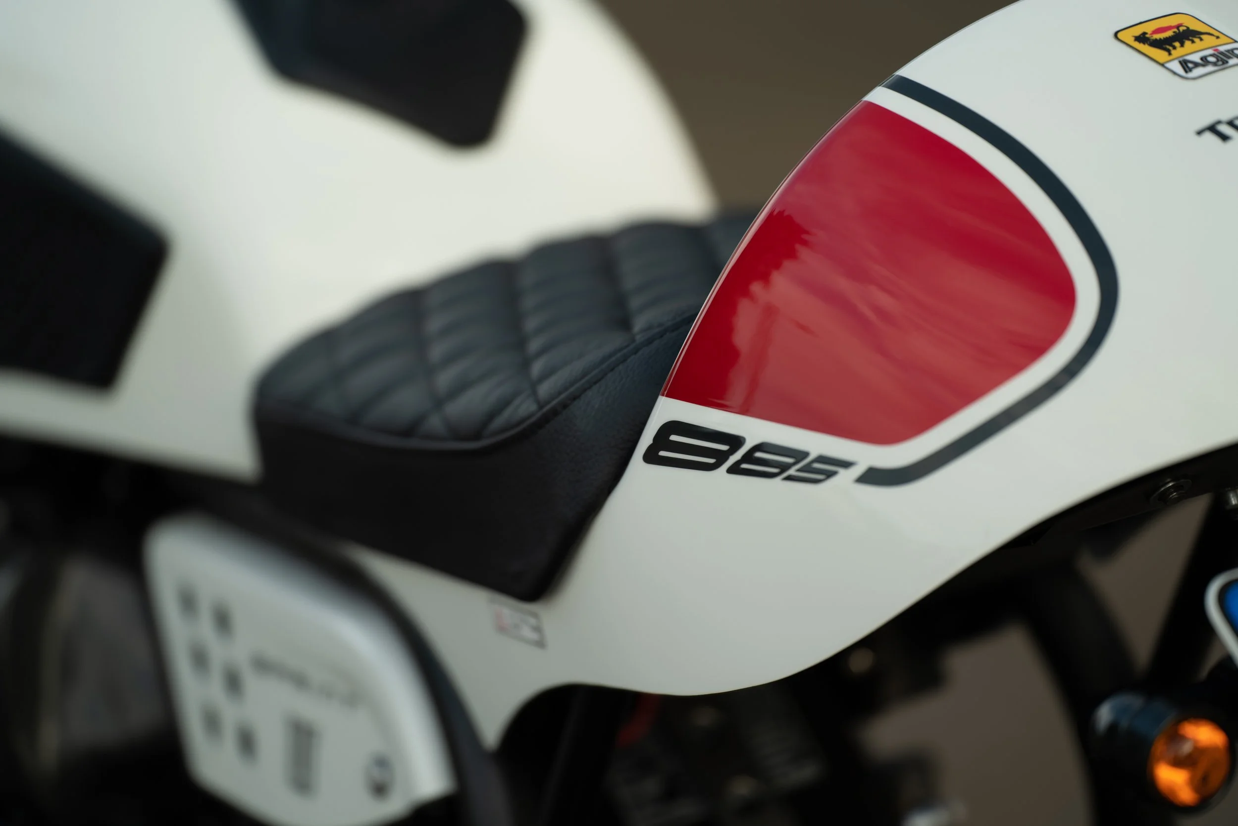 Close-up of a white motorcycle with black seat and red and black decal that reads '885'.