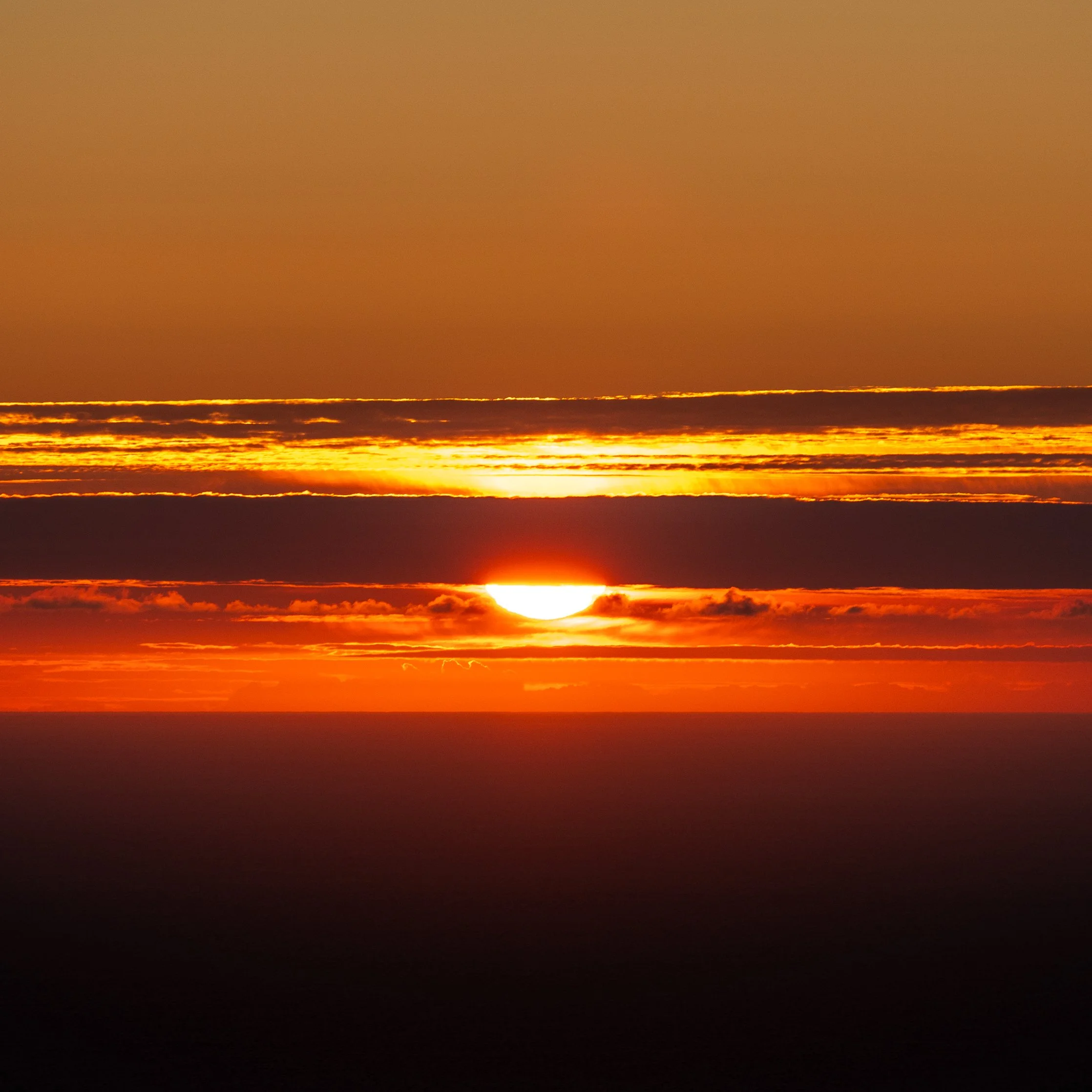 Sunset over the ocean with an orange sky and scattered clouds near the horizon.