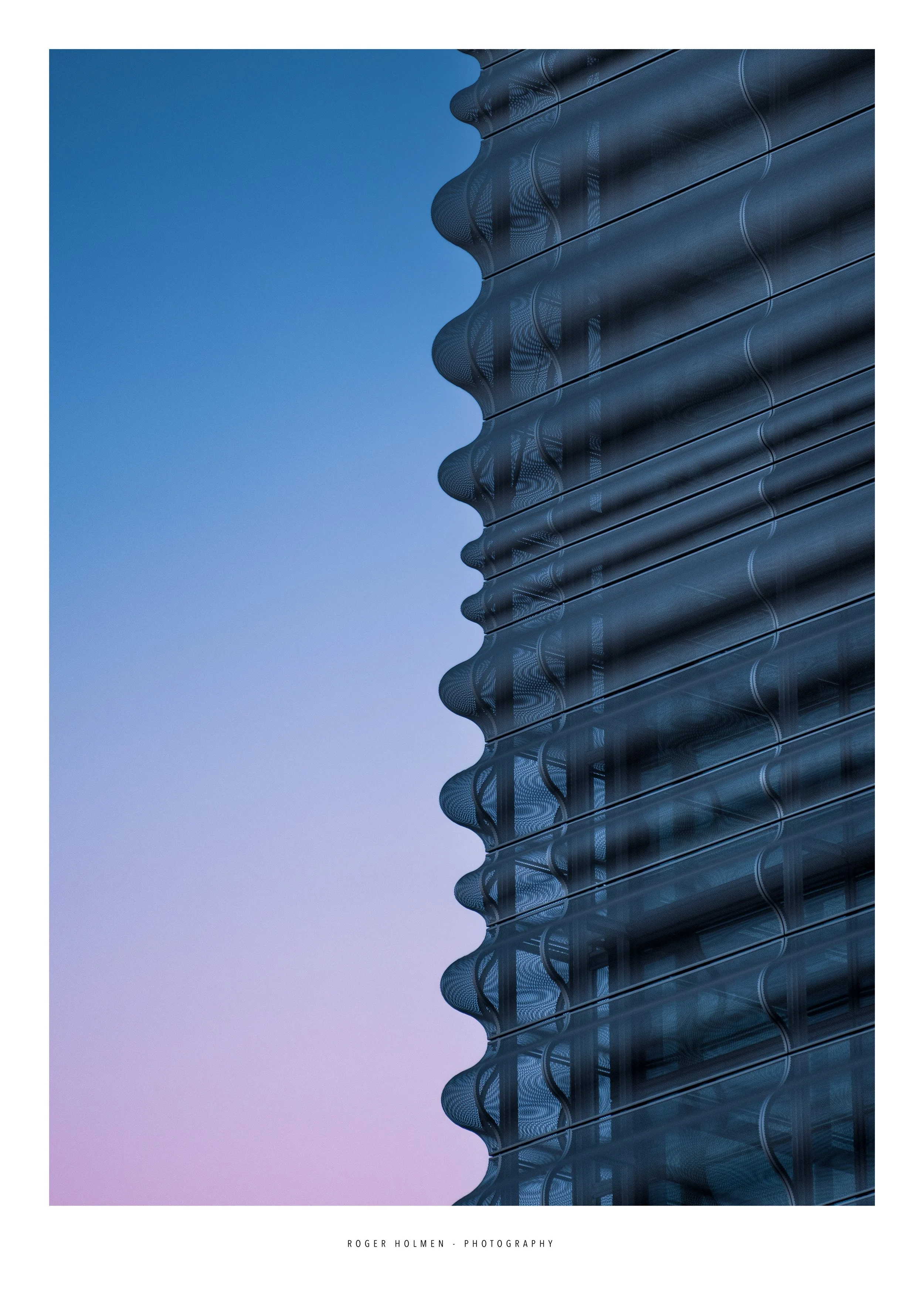 Close-up of a modern glass building with a reflective curved facade against a clear blue and purple sky