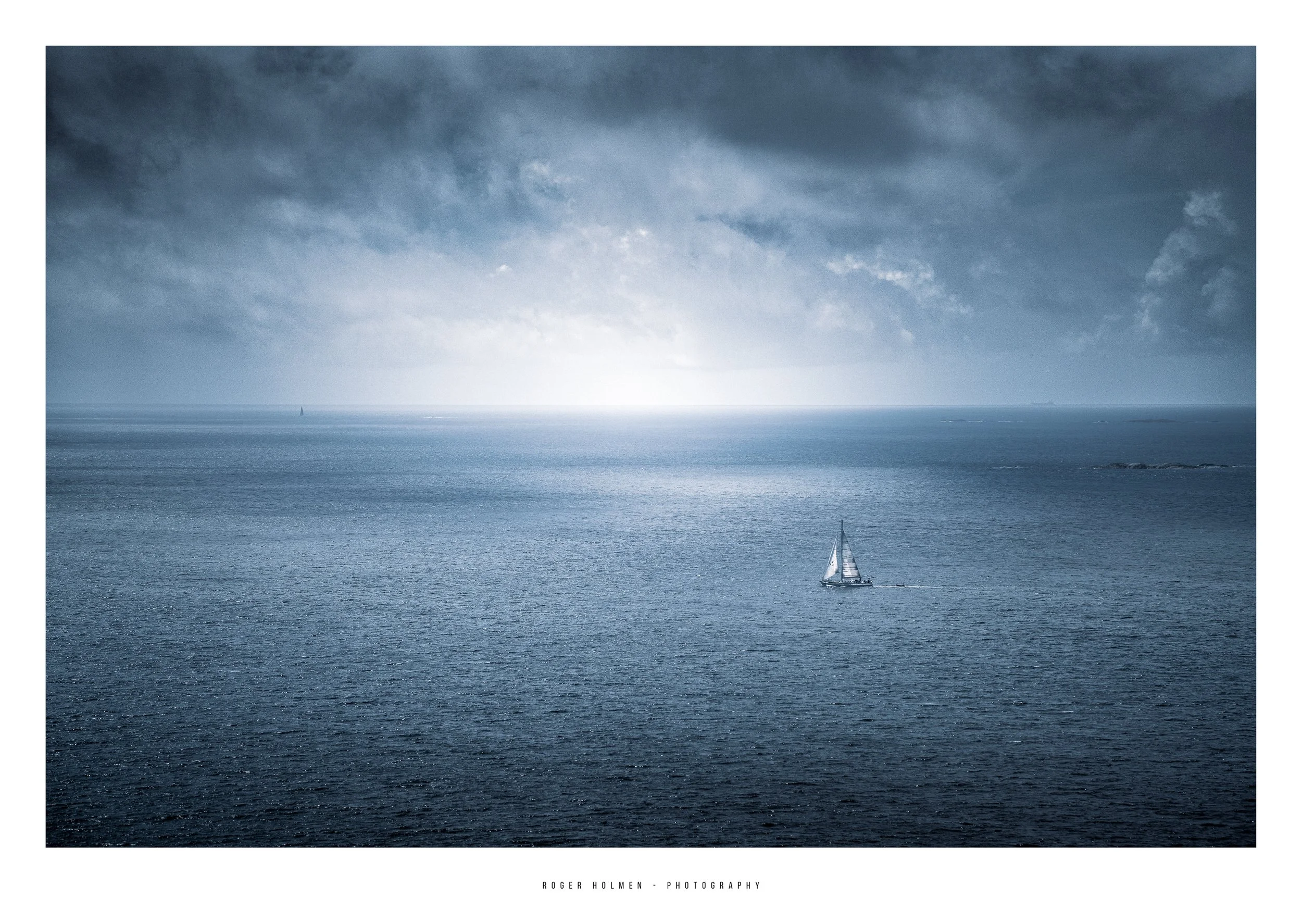 A sailboat on the ocean under a cloudy sky, with the horizon visible in the distance.
