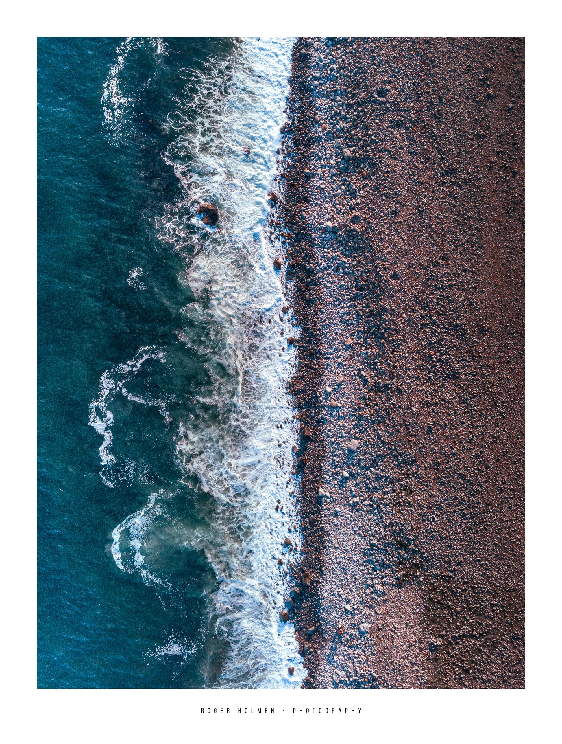 An aerial view of a rocky shoreline with ocean waves crashing onto the beach.