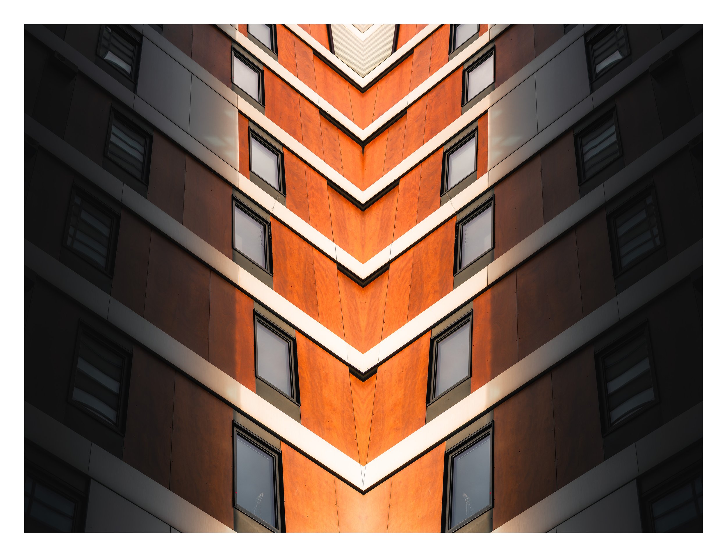 A modern building with a distinctive geometric pattern created by overlapping triangles in orange and gray, with multiple rectangular windows. Barcode Oslo. Arkitektur foto.