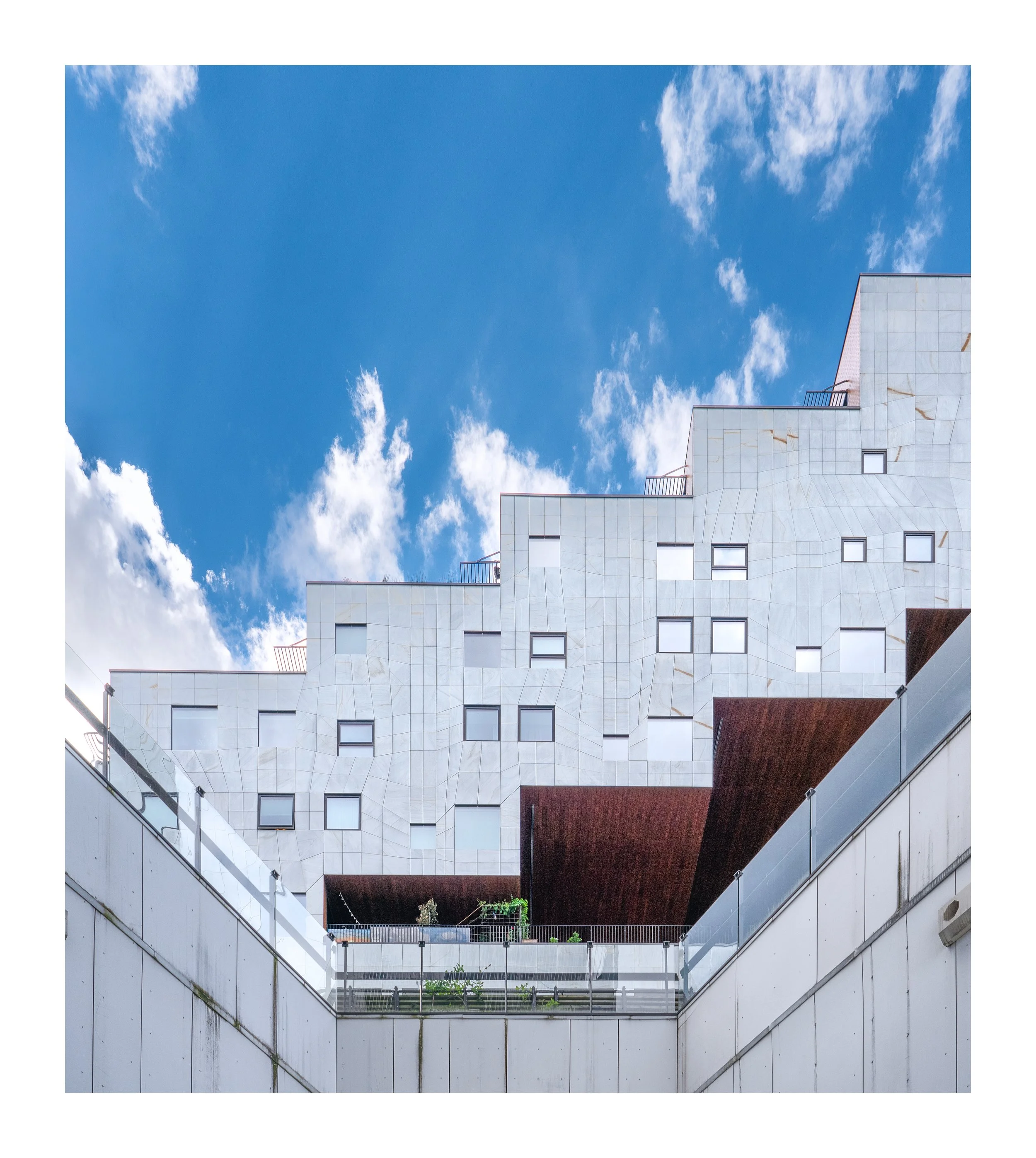 View of a modern multi-story building with a white facade, windows, balconies with plants, and a blue sky with scattered clouds above. Barcode Oslo. Arkitektur foto.