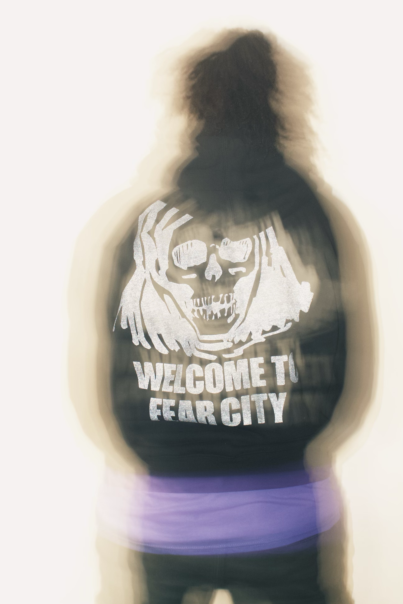 Person wearing a hoodie with a graphic of a skull with dreadlocks and the text "WELCOME TO FEAR CITY".