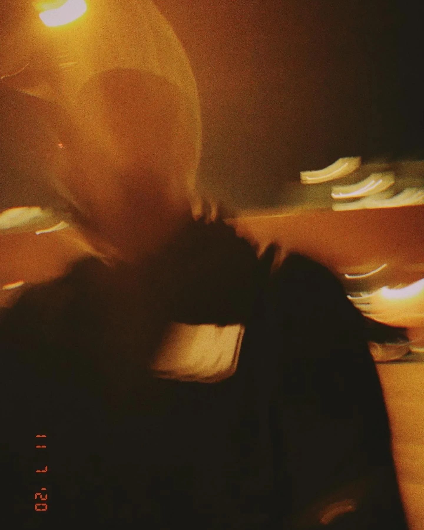 A person wearing a dark jacket is holding a large orange balloon in a dimly lit indoor space with warm lighting.