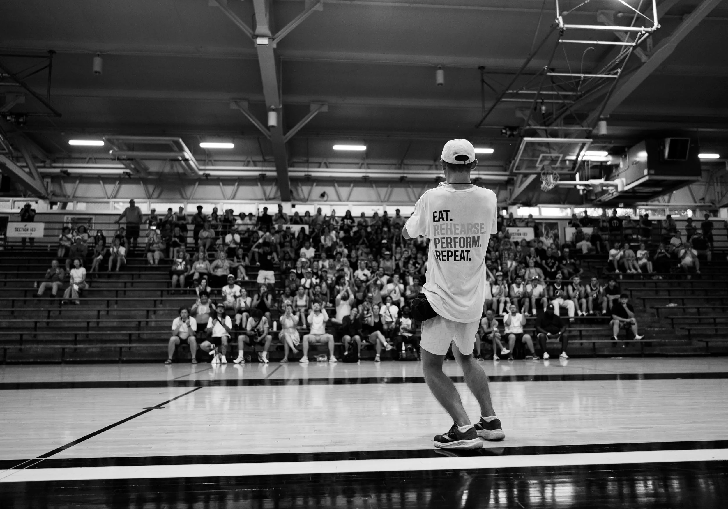 Photo of performer playing to a crowd on indoor bleachers.