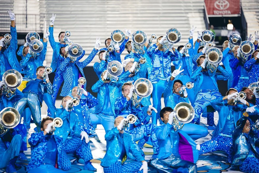 Action shot of brass members crowding together and playing their instruments while posing.