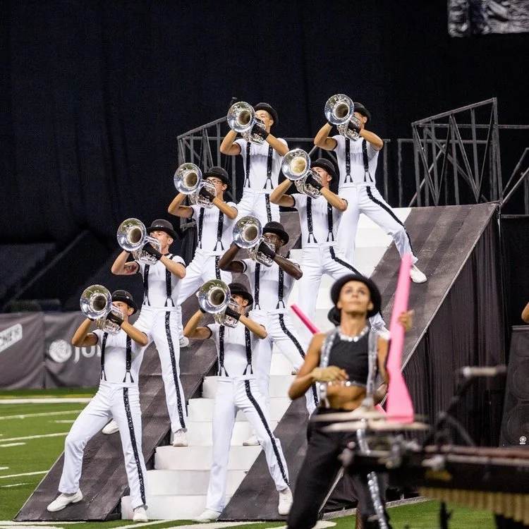 Baritones and euphoniums standing and playing on front staircase of large jagged line set piece.
