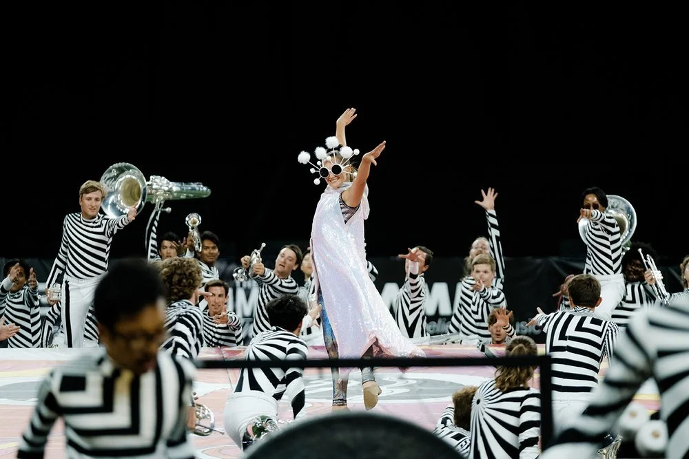 Action shot of color guard member wearing 'Lucy' sunglasses and a sparkly dress.