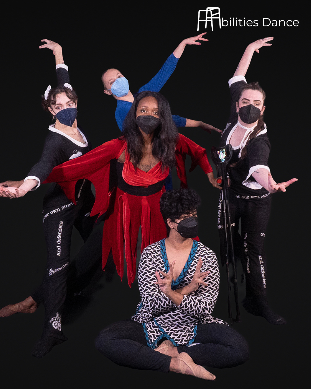 Firebird Part 2 shoot with Claire and Dara at sides reaching one arm in front and one arm up . They’re wearing black jumpsuits with words in random places. Amaal seated with wrists crossed and hands outward. He’s wearing a chevron print blouse with 