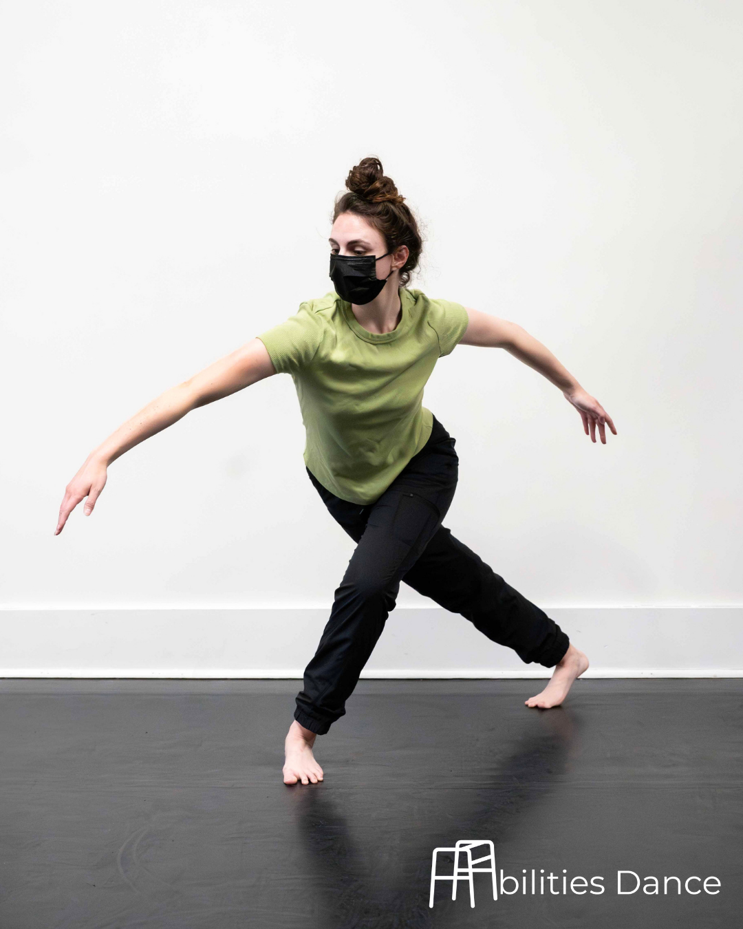 Image of Tori in a green top and black leggings in a deep lung with arms curved down