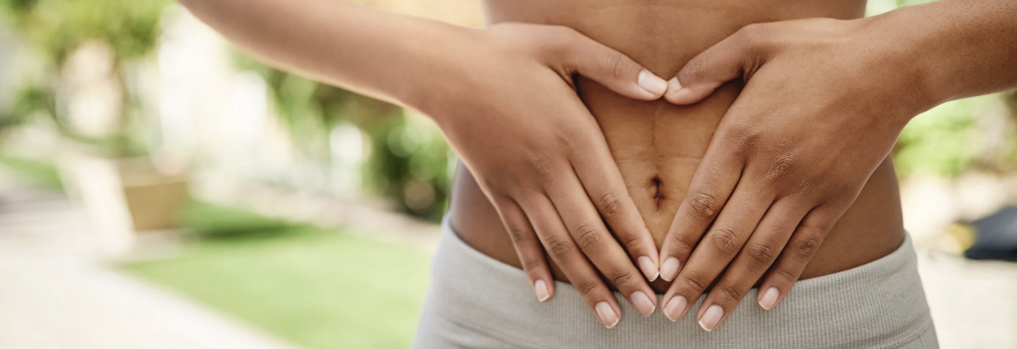 Close-up of hands forming a heart over the abdomen, representing gut health, digestive balance, and holistic wellness.