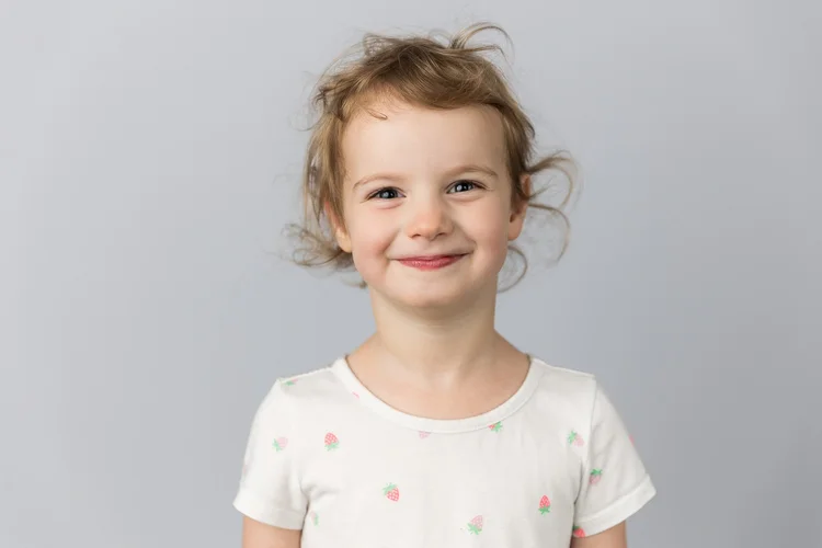 Child smiling in a white shirt against a light gray backdrop