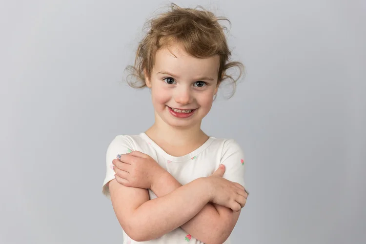 Child smiling with folded arms against a light gray backdrop