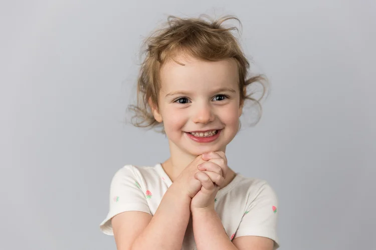 Child smiling with hands beneath their chin