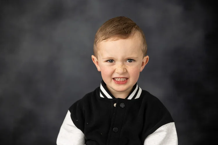 Child smiling in a varsity jacket against a charcoal backdrop