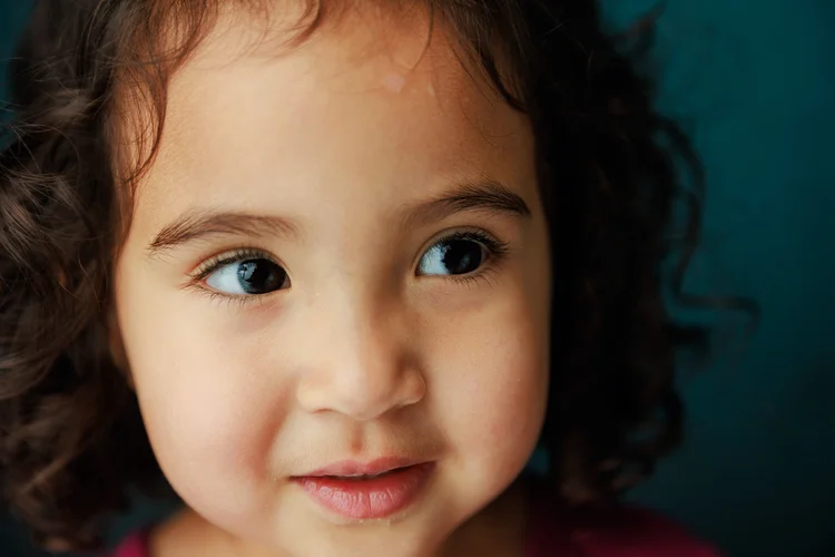 Close-up portrait of a child against a teal backdrop