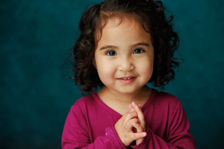 Child holding their hands together against a teal backdrop