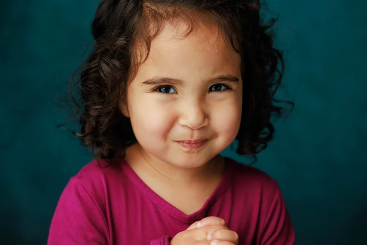 Child smiling in a magenta shirt against a teal backdrop