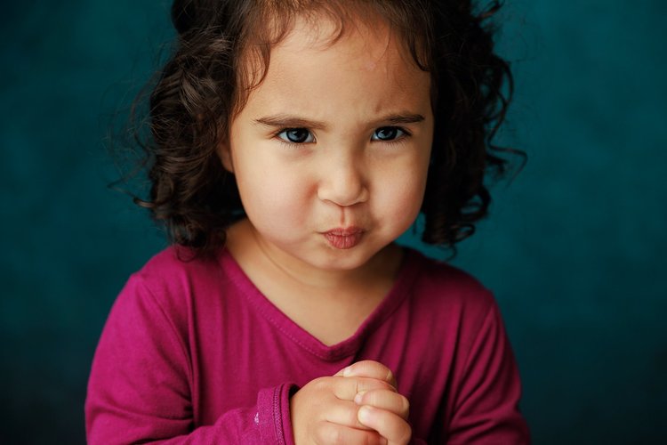 Child with a thoughtful expression against a teal backdrop