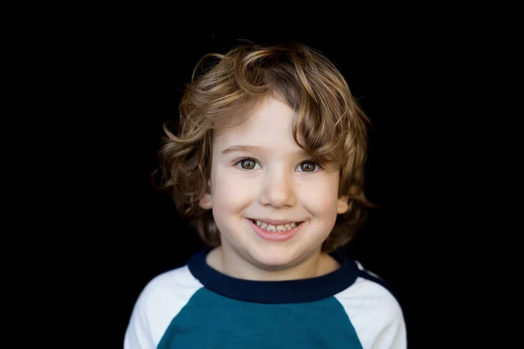 Student smiling in a blue and white shirt against a black backdrop