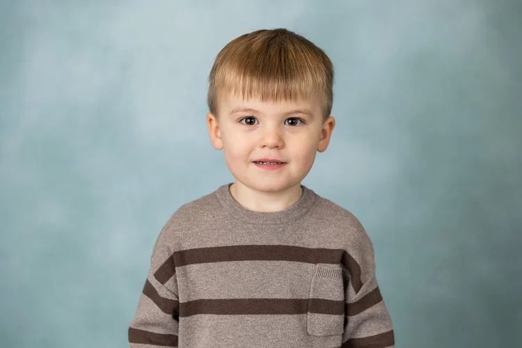Child smiling in a striped sweater against a pale blue-green backdrop