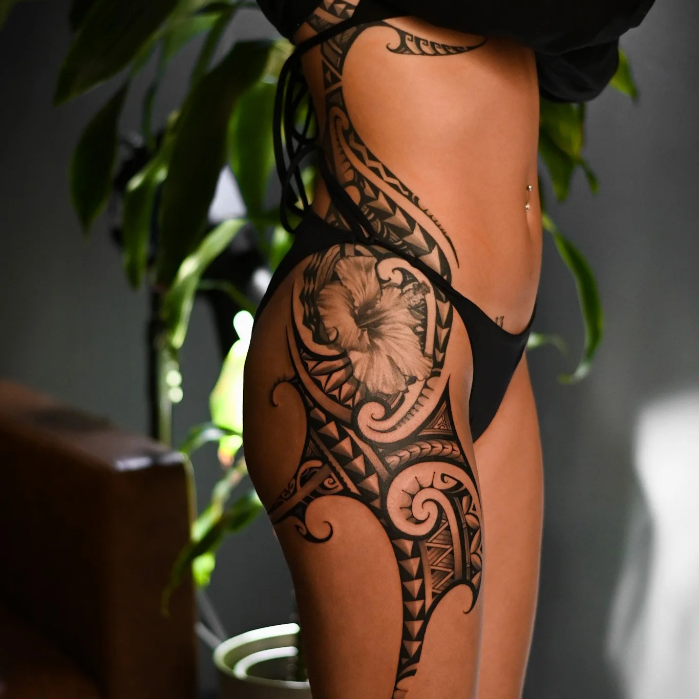 Close-up of a woman's side showing detailed Polynesian-style tattoos on her leg, hip, and torso
