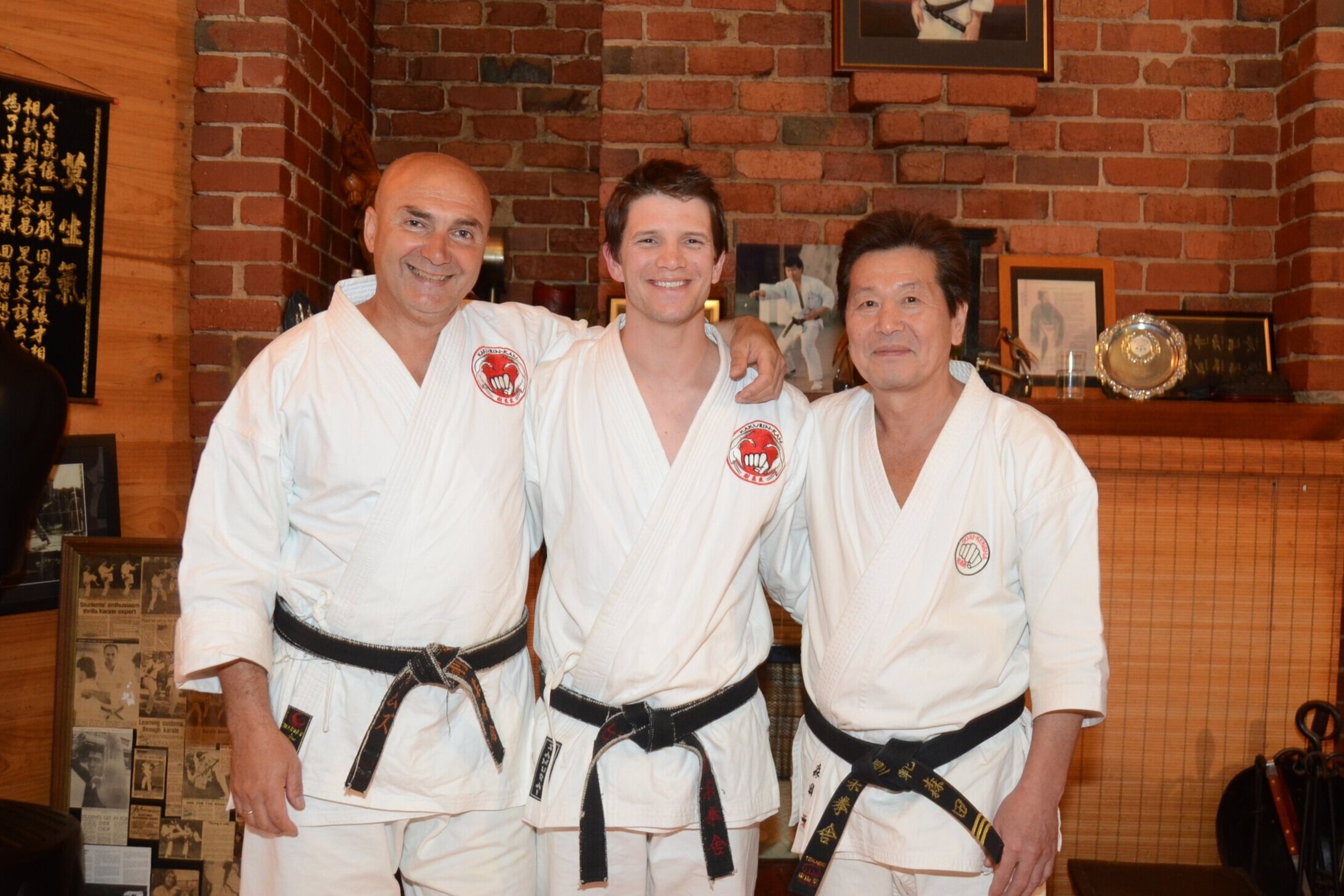 Goju Ryu Karate masters James Sumarac and Morita Toshio embracing Peter Zarb