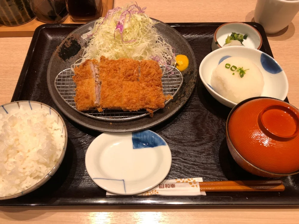 A set meal from Wakou. Tonkatsu on-top of a wire net, Served with chopped raw cabbage, rice, miso soup, grated radish, and pickles on the side.