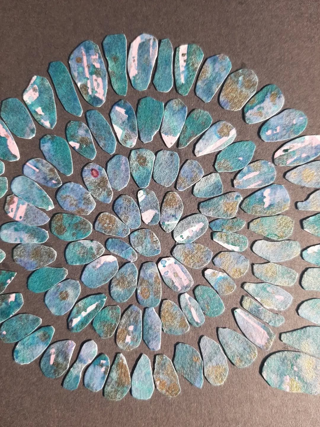 An #Ammonite spiral with beautiful colours of teal, green, shots of pink, and gold ink. Mounted on a dark backing board. Made up of small individual pebbles, smaller than I usually use.
It measures approximately 19x18 cm. 
It's available for &pound;6
