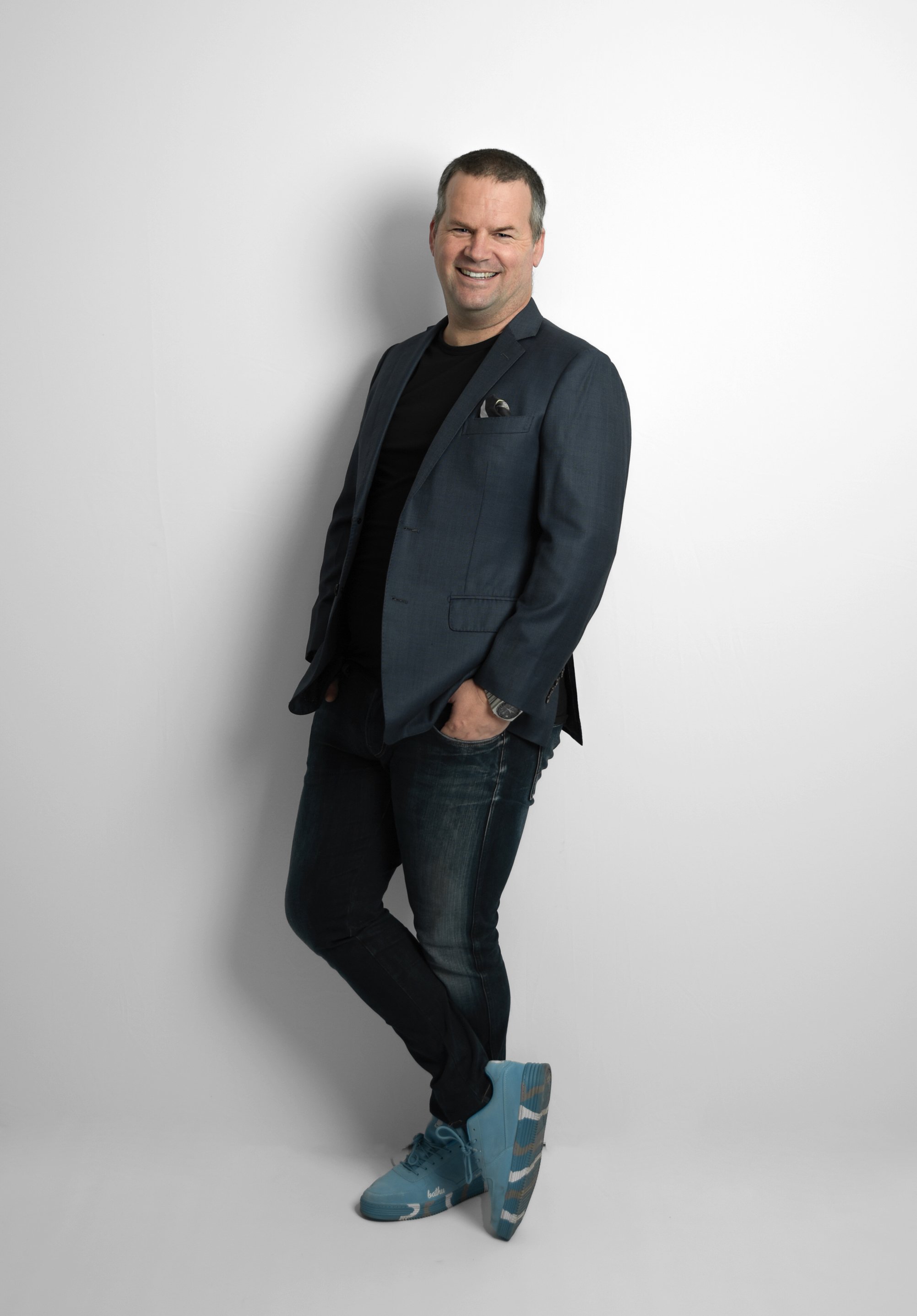 Brendan le Grange leaning against a white wall in a studio, smiling
