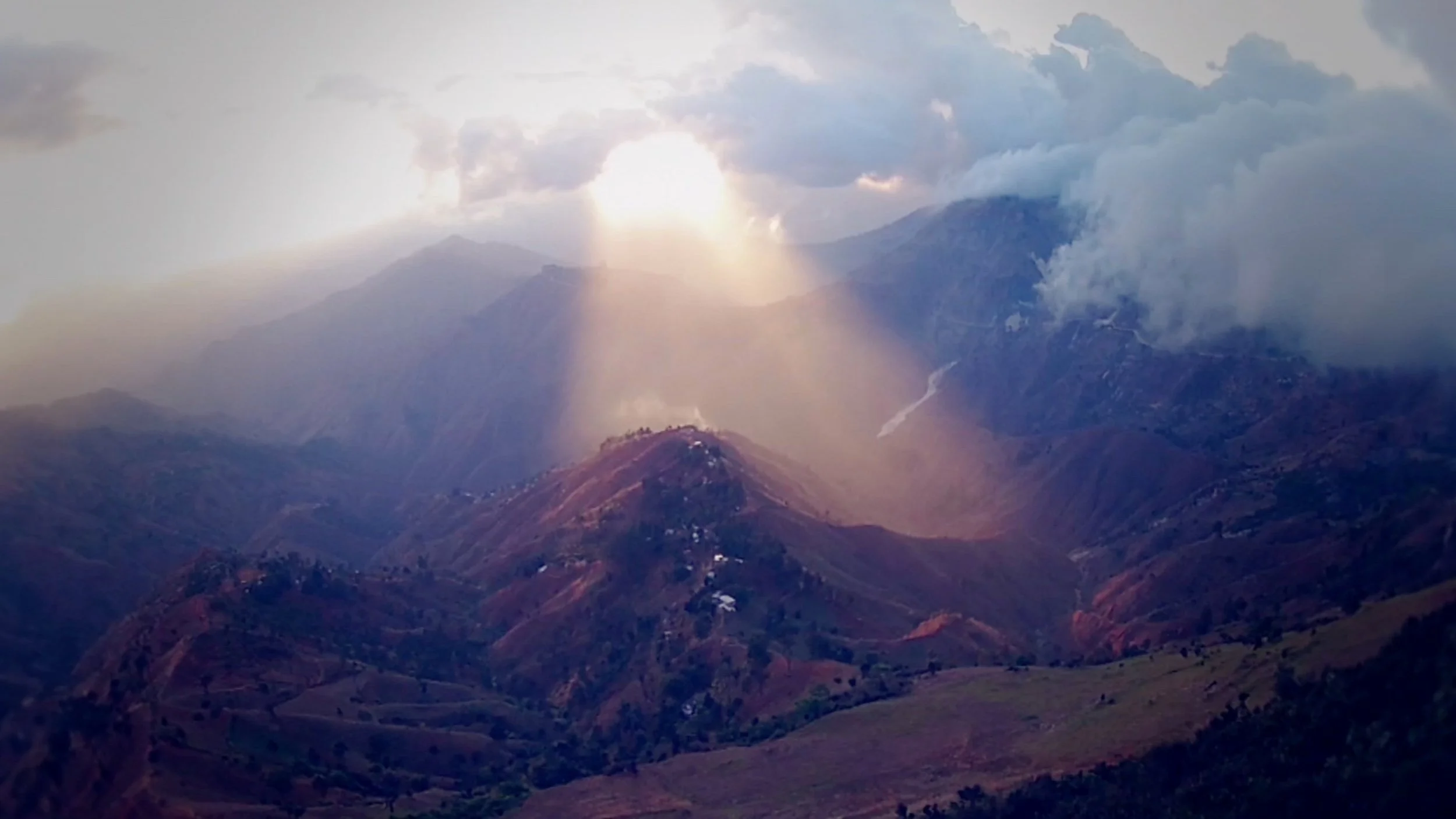 sun breaking through clouds onto hills like beam of light from Heaven