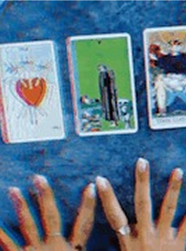 Three tarot cards laid out on a blue surface with two hands below them.